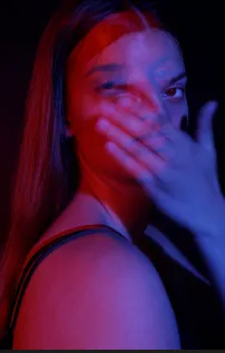 Portrait of a woman with a hand over one eye, lit in red and blue